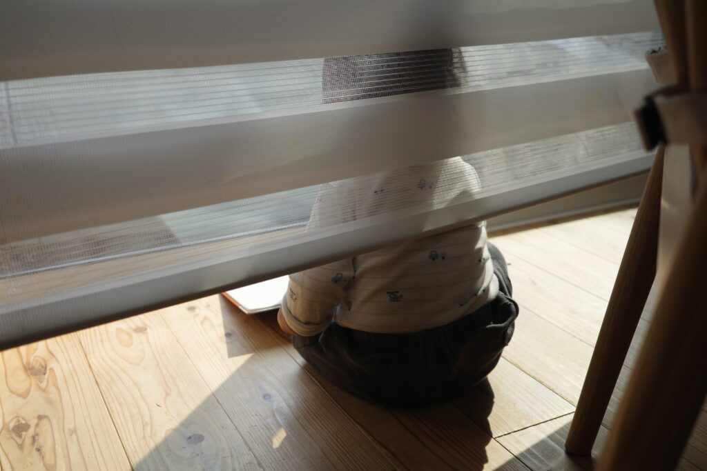 カーテンの裏に隠れていたずらをする子どもの画像