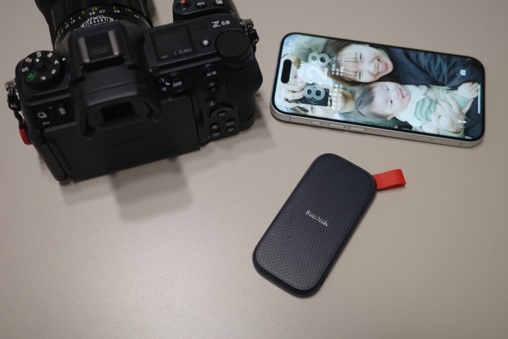 カメラとiPhoneとサイズ感を比較するサンディスクポータブルSSDのイメージ